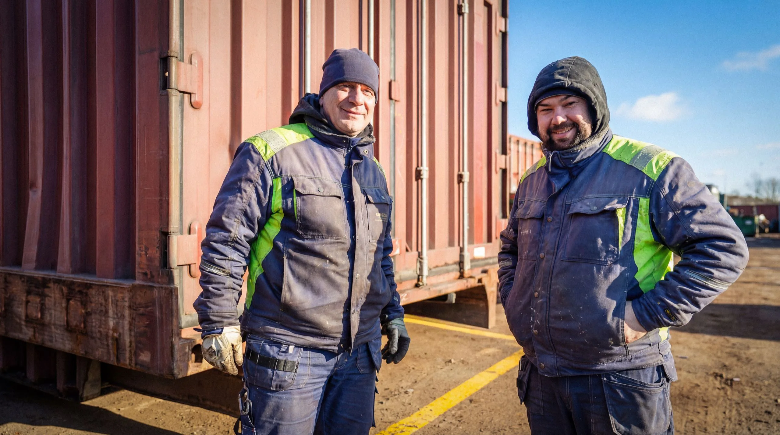 Två Elfcon-medarbetare står framför en röd fraktcontainer.